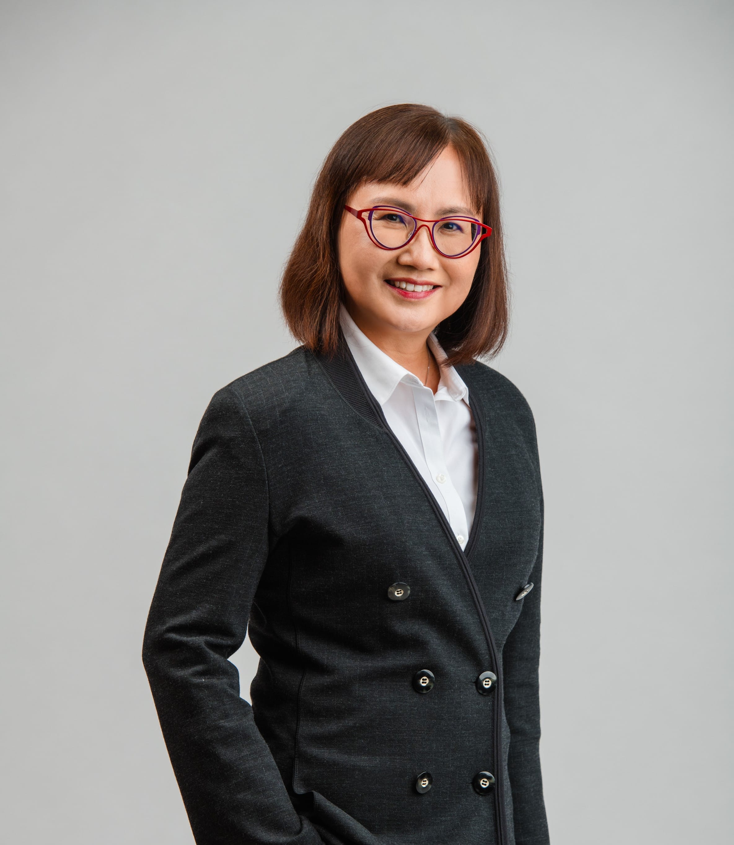 Shoulder-up shot of a woman with red glasses, wearing a white blouse and dark gray jacket.